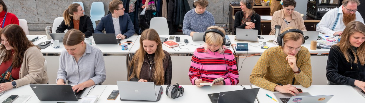 an langen Tischen sitzen Podcaster:innen auf der Leipziger Buchmesse 2023 und arbeiten an ihren Laptops