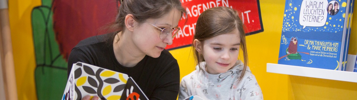 Frau und Mädchen lesen gemeinsam ein Bilderbuch auf der Leipziger Buchmesse 2024