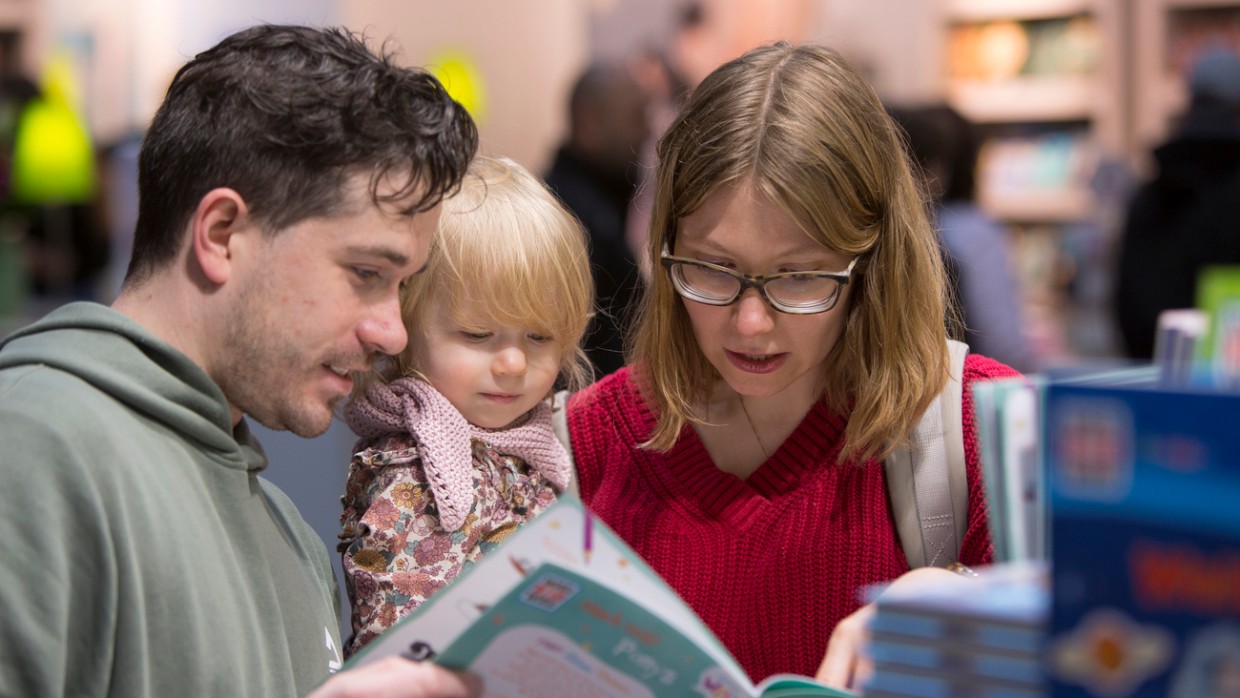 Frau, Mann und Kind schauen gemeinsam in ein Buch auf der Leipziger Buchmesse 2024