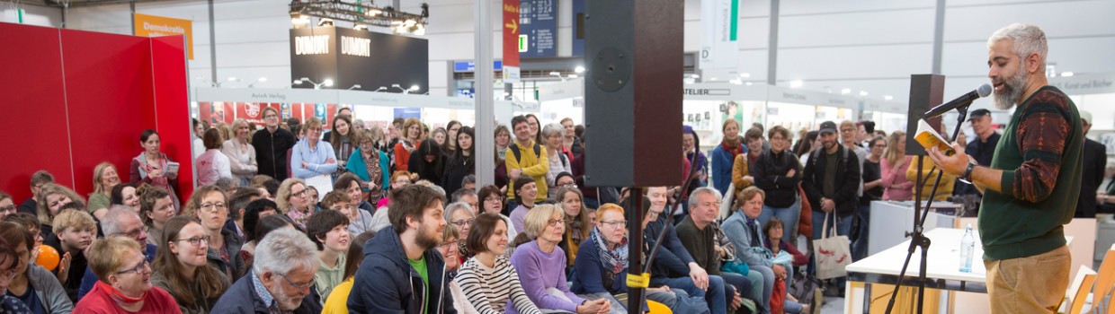 Lesung auf einer Bühne vor vollbesetztem Publikum während der Leipziger Buchmesse 2024