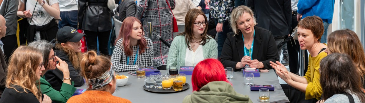 Tischgespräch mit mehreren Teilnehmerinnen in einer Messehalle auf der Leipziger Buchmesse 2024