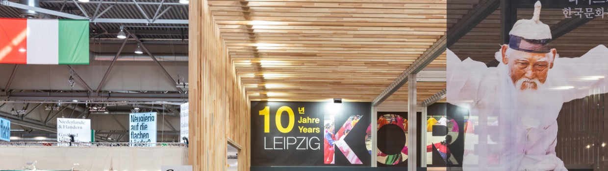 Ausstellungshalle mit koreanischem Messestand und italienischer Flagge während der Leipziger Buchmesse 2024 mit viele Besucher:innen an Messeständen