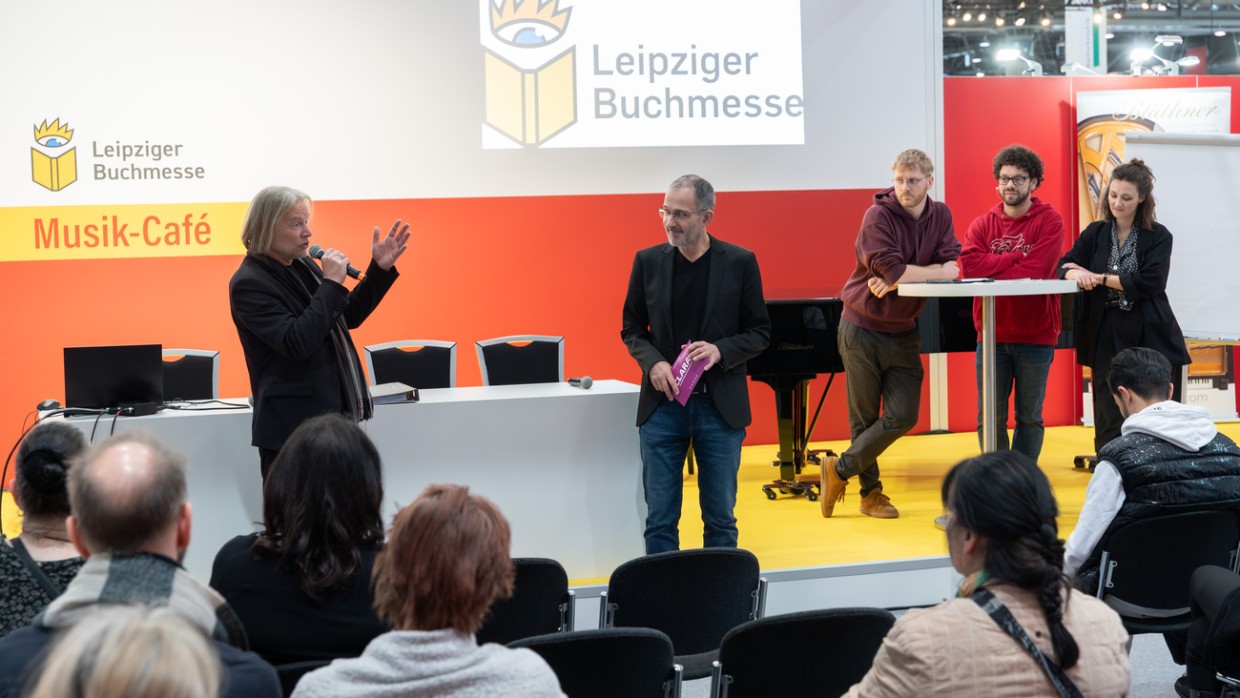 mehrere Personen auf der Bühnedes Musik-Café vor vollbesetztem Publikum während der Leipziger Buchmesse 2024
