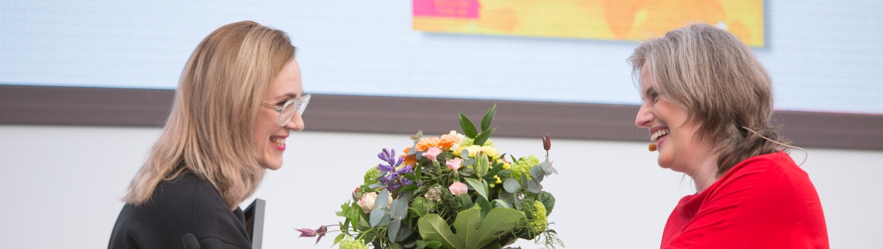 Jurorin Insa Wilke überreicht der Gewinnerin Barbi Marković einen Blumenstrauß am Rednerpult bei der Verleihung vom Preis der Leipziger Buchmesse 2024